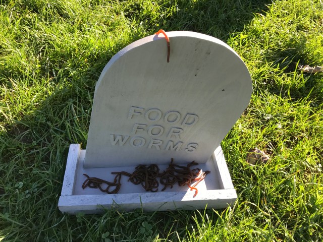 A gravestone saying 'Food for worms' filled with worms.